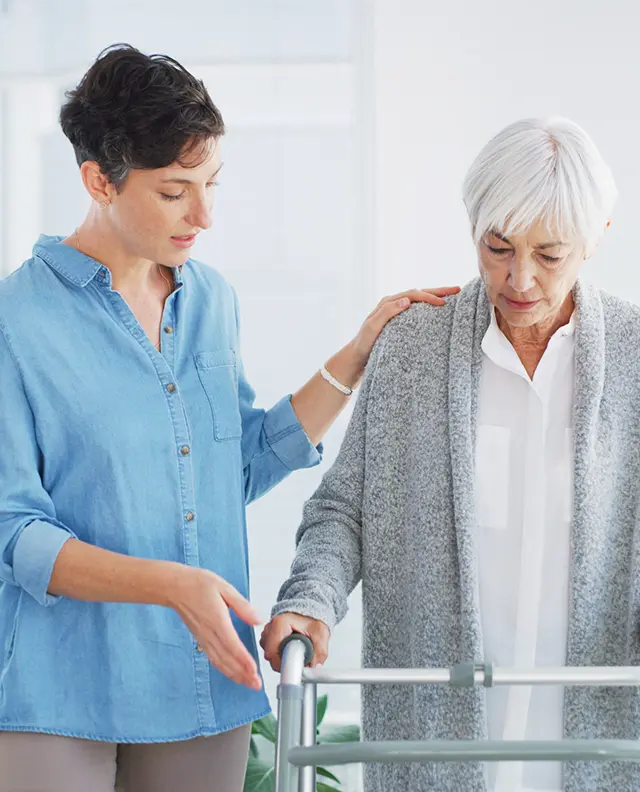 An occupational therapist supports an older woman using a walker during a rehabilitation session at Katmai Eye and Vision Center, focusing on improving daily function and independence.